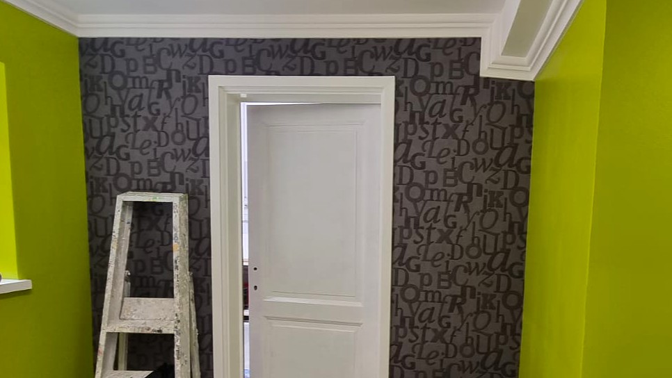 Mur peint en vert anis avec tapisserie grise à motifs typographiques et porte blanche