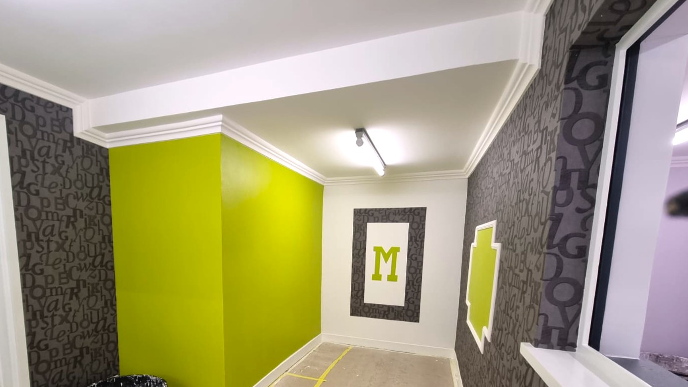 Couloir décoré avec mur vert anis, tapisserie grise à motifs et cadres décoratifs