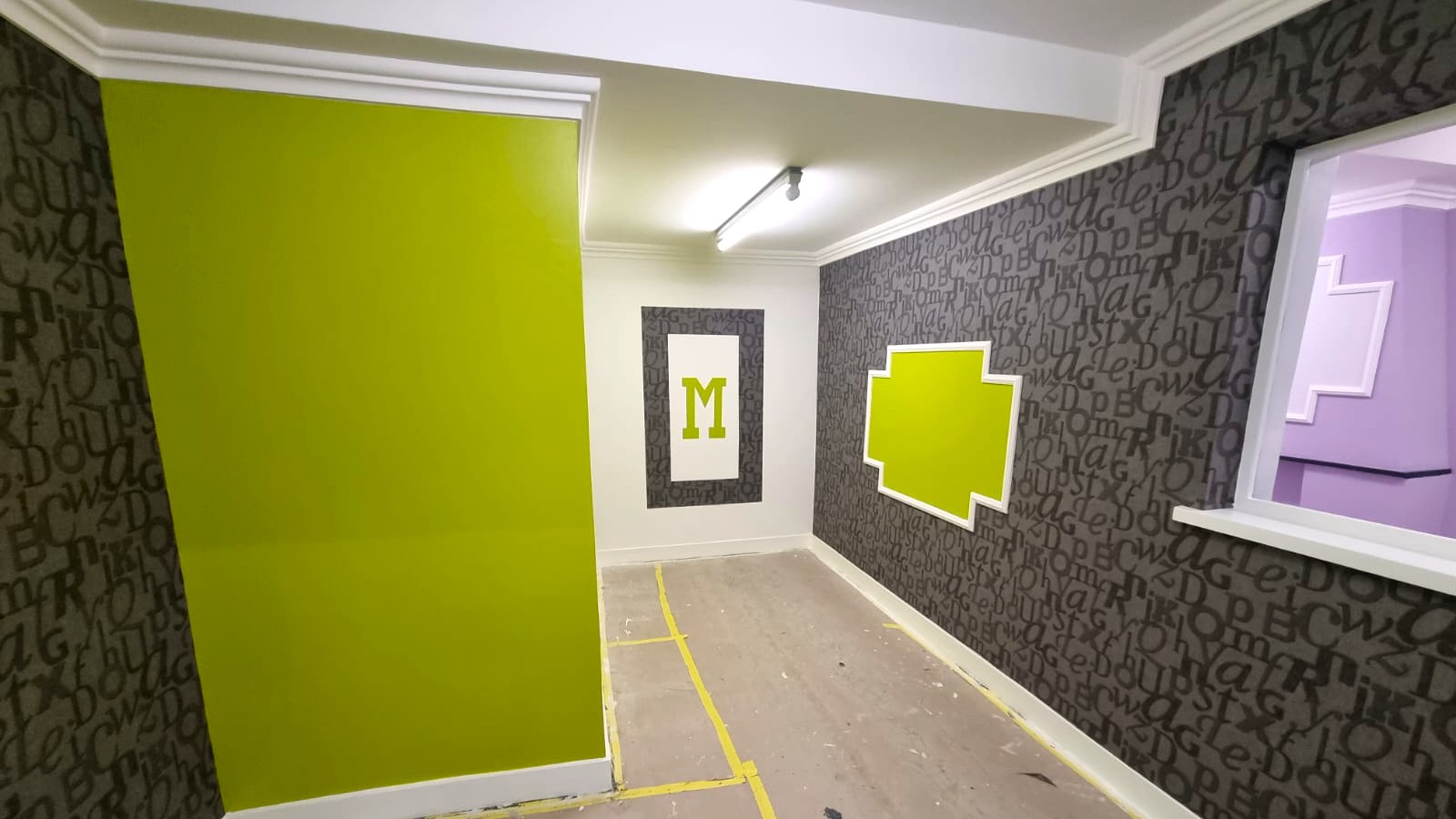 Couloir décoré avec mur peint vert anis, tapisserie grise à motifs typographiques et cadre mural décoratif